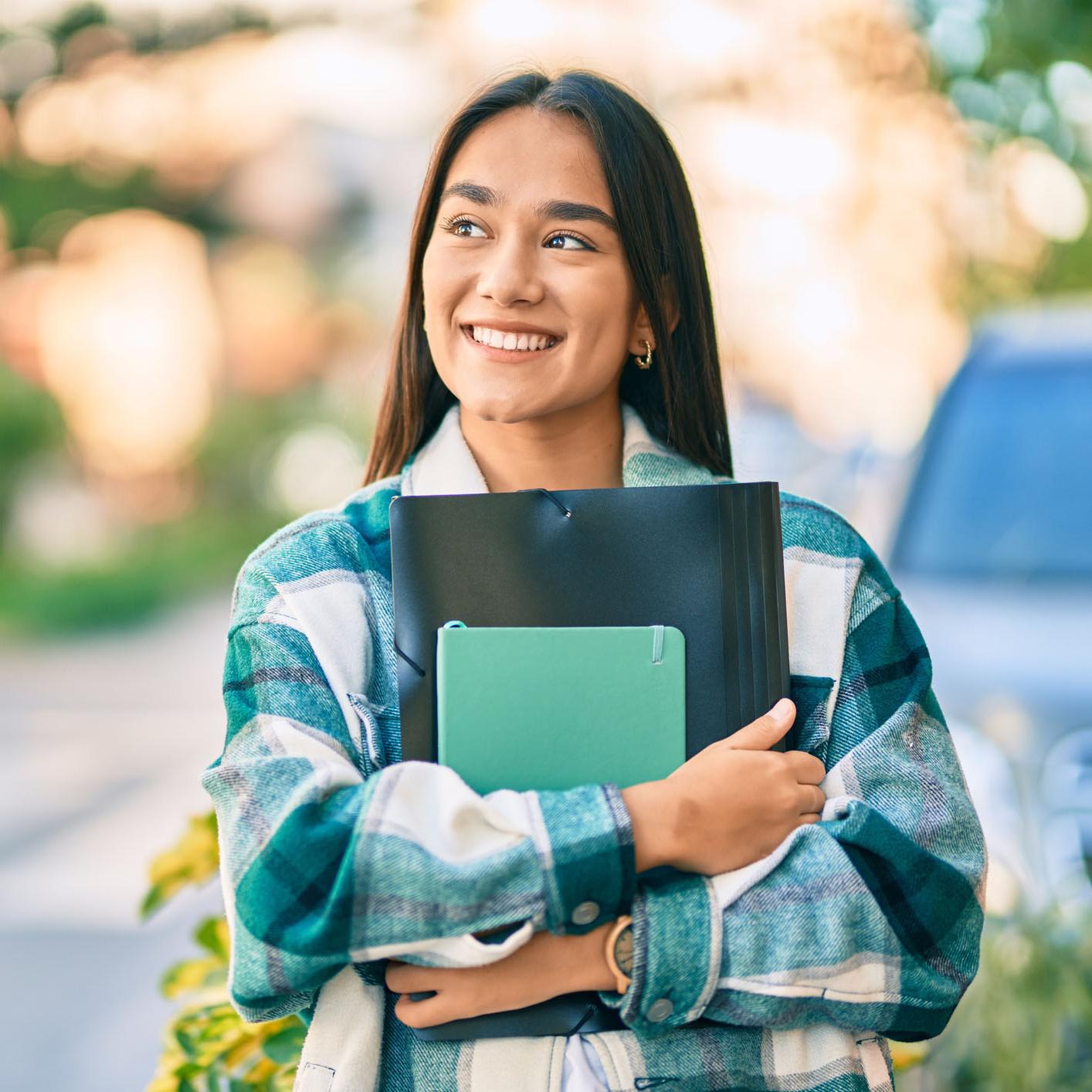 A smiling college student carrying a notebook.